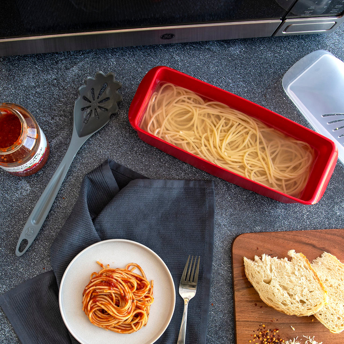 Nordic Ware microwave pasta cooker with vented lid, shows quick-drain capability.